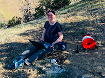 Dr. McMillan sitting on hillside with equipment
